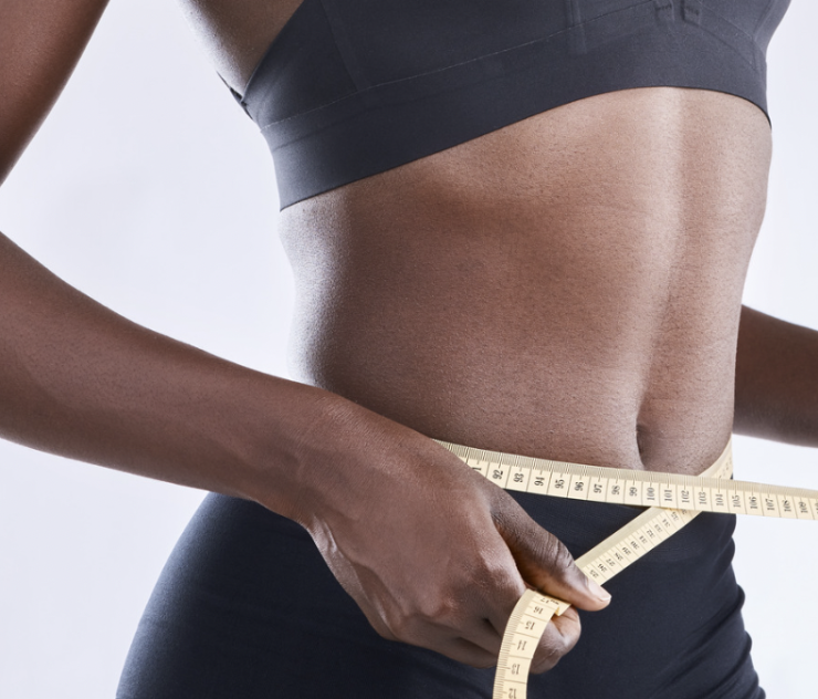 A woman is measuring her waist with a tape measure.